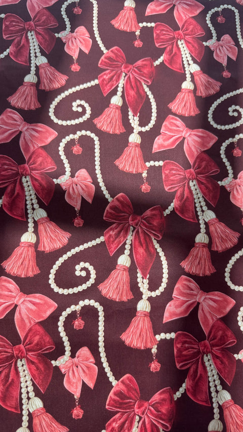 Close-up of Veloura cotton satin fabric showing pink bows, pearl strands and tassels